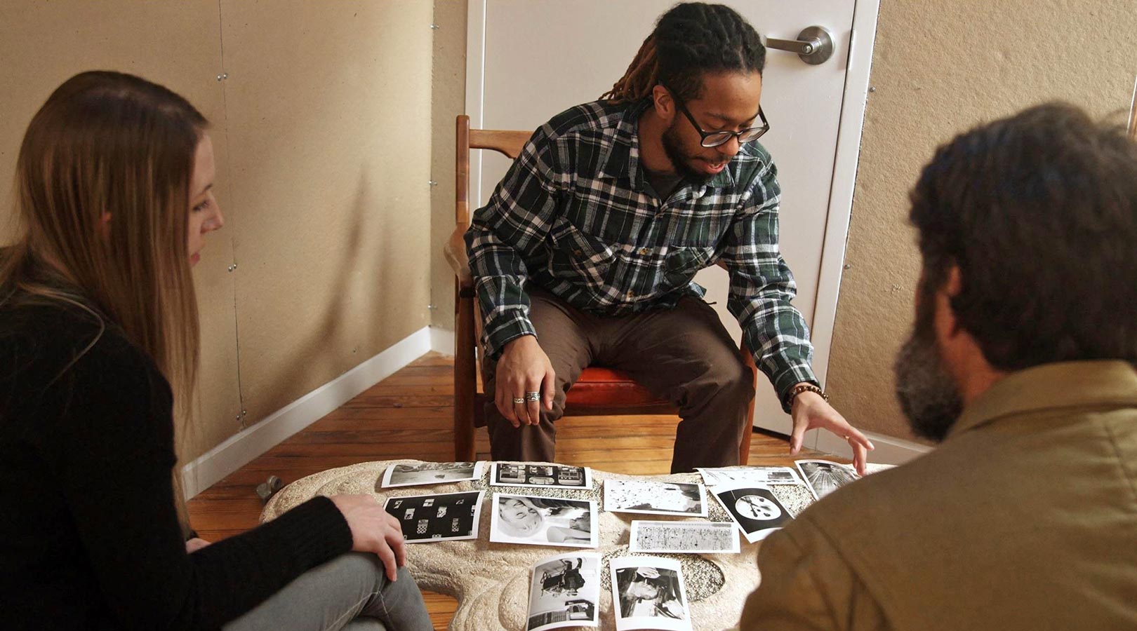 Three people in conversation, looking at photographs spread on a low table